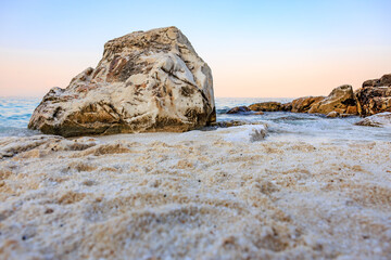 A large rock sits on a beach with a beautiful blue sky in the background