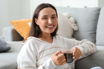 Sticker - Happy young woman with glass cup of hot cocoa in living room