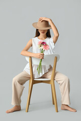 Wall Mural - Beautiful young woman with gerbera flowers sitting on chair against grey background