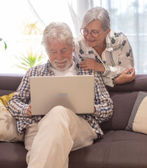 Sticker - Relaxed senior white haired couple sitting on home sofa using computer have fun together enjoying happy retirement lifestyle in good mood