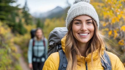 A smiling woman in a yellow jacket and grey beanie enjoys a hike among vibrant autumn trees, capturing the essence of joy and connection with nature.