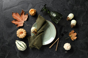 Beautiful table setting with fresh pumpkin, skulls, autumn leaves and burning candles for Halloween celebration on black background