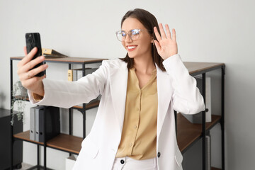 Wall Mural - Young businesswoman with mobile phone video chatting in office