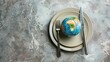 © Ahmad-Muslimin - A globe on a plate with a fork and knife, symbolizing the consumption of the Earth