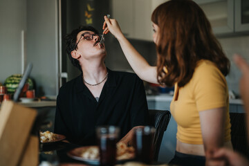 Wall Mural - A young couple enjoys a playful moment while sharing a meal at home. The scene captures intimacy and joy in a casual dining setting, highlighting companionship and happiness.