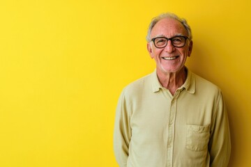 Half body shot of a cheerful older man, wearing glasses, standing against a solid yellow background with room for messaging