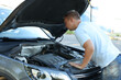 © New Africa - Stressed man looking under hood of broken car outdoors