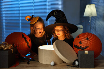 Canvas Print - Surprised children in costumes with festive decor and gift boxes indoors at night. Halloween celebration