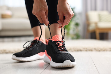 Canvas Print - Woman tying shoelace of sneaker indoors, closeup. Space for text