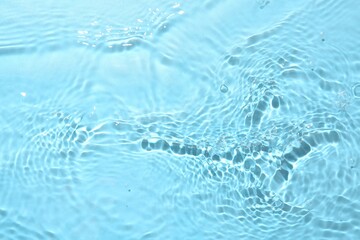 Rippled surface of clear water on light blue background, closeup