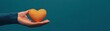 © Chanoknan - A hand holding a vibrant orange heart symbolizing love, care, and affection against a calming teal background.