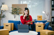 © Parichat - Young entrepreneur taking notes on a clipboard while checking her online shop orders on a digital tablet, surrounded by cardboard boxes