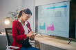 © Parichat - Young professional is taking notes while reviewing data displayed on a large screen, showcasing the modern approach to business analysis