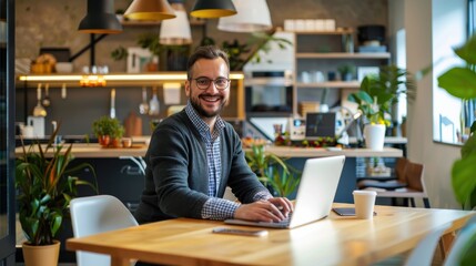 Fototapete - A man is sitting at a table with a laptop and smiling