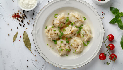 Wall Mural - Dumplings boiled in chicken broth and sprinkled with green onions on a white plate. Cherry tomatoes, peppercorns and bay leaves on a light table. Sour cream in a white bowl in the background. Top view