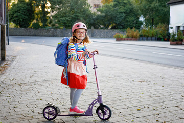 little happy girl on way to school by pushing scooter. elementary school child riding in the city, w