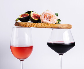 Two glasses with red and rose wine balancing wooden board with ripe figs and pink rose