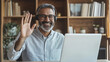 © forenna - An Indian Arabian mature businessman wearing wireless earphones, waving and giving a greeting gesture while looking at his personal teacher during an online webinar, showcasing the