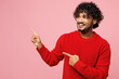 © ViDi Studio - Young smiling happy Indian man he wear red sweater casual clothes point index finger aside indicate on area mock up isolated on plain pastel light pink background studio portrait. Lifestyle concept.