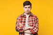 © ViDi Studio - Young sad mad upset frowning grumpy man he wears red checkered shirt casual clothes hold hands crossed folded look camera isolated on plain yellow orange background studio portrait. Lifestyle concept.