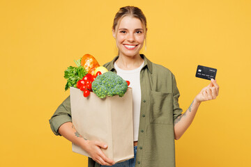 Poster - Young smiling fun woman wear casual clothes hold bag for takeaway mock up with food products, mock up of credit bank card isolated on plain yellow background. Delivery service from shop or restaurant.