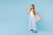 © ViDi Studio - Full body young woman wear casual clothes hold in hand paper package bags after shopping point index finger aside on area mock up isolated on plain blue background. Black Friday sale buy day concept.