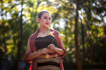 A portrait of a smiling woman in a summer park, surrounded by green trees, wearing traditional Thai fashion and enjoying the beauty of nature.