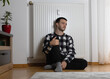 © Kateryna - The guy is sitting on the floor with his back pressed against the radiator. Cold weather and the heating season