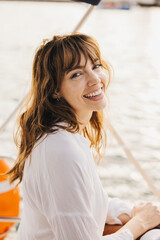 A cheerful woman with brown hair smiling while sitting on a boat. She's enjoying a sunny day on the water, creating a joyful and relaxed atmosphere.