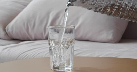 Poster - Pouring fresh water from jug into glass on wooden table in room