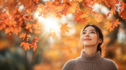 Wall Mural - A woman is standing in a field of autumn leaves, looking up at the sun