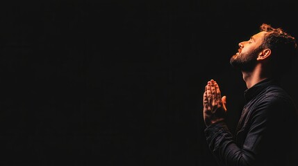 A solitary man engaged in prayer, illuminated softly against a dark backdrop, embodying a moment of reflection and spirituality.