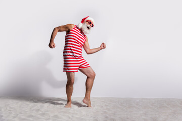 Wall Mural - Photo of cheerful santa claus wear red striped swimwear dancing empty space isolated on white sandy beach background