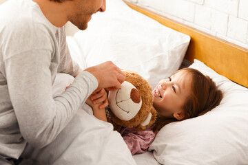 Wall Mural - Little girl lying in bed in the morning, happy to see her dad, family morning