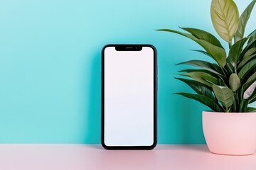 Wall Mural - A sleek smartphone stands against a turquoise background, accompanied by a green plant in a white pot, creating a modern and fresh aesthetic.