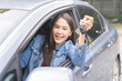 © KMPZZZ - Dealership automobile, smile asian young woman, happy girl sitting in new car after purchase success, showing, holding auto remote key of vehicle, owner driver female buy gift for yourself at showroom