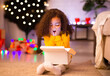 © Prostock-studio - Desired present. Amazed little afro girl opening Christmas gift near xmas tree, free space