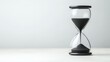 © Tasaneewalai - Minimalist Serenity Elegant Black Sand Hourglass on White Surface - Conceptual Timepiece for Efficiency and Focus