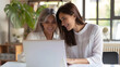 © sakir - Two happy busy female employees working together using computer planning project. Middle aged professional business woman consulting teaching young employee looking at laptop sitting a. generative ai.