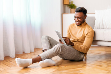 Sticker - Weekend Concept. Cheerful Afro Guy Using Digital Tablet And Smiling Sitting On Floor At Home. Selective Focus