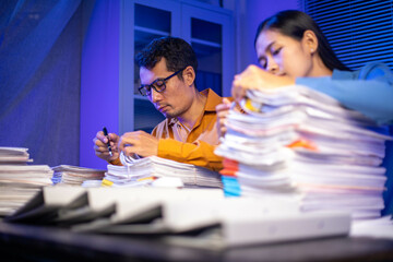 Image of businessman working hard in front of many documents on desk at office late at night with serious action. Concept of working hard and too late.