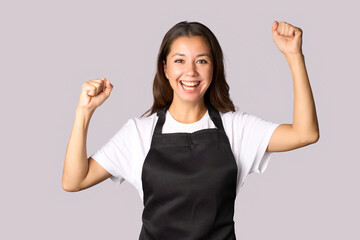 portrait of cheerful woman wear apron with raised hands, celebrating success