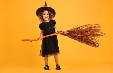 Wall Mural - Funny girl with broom dressed like witch on yellow background. Halloween celebration