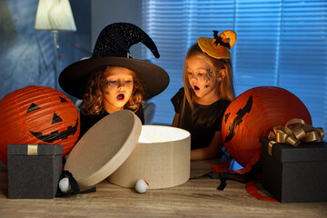 Wall Mural - Surprised children in costumes with festive decor and gift boxes indoors at night. Halloween celebration