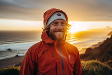 Sticker - Portrait of a happy man in his 20s wearing a windproof softshell in stunning sunset beach background