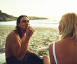 © StarDweller/peopleimages.com - Couple, happy and eating on beach for picnic, love and milestone in relationship at sunset. Man, woman or sharing food at ocean for bonding, summer vacation or pizza in evening on sand in Australia