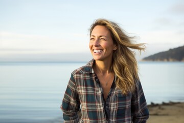 Canvas Print - Portrait of a grinning woman in her 40s wearing a comfy flannel shirt in front of calm bay background