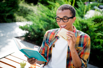 Canvas Print - Portrait of nice young man sit bench eat sandwich read book wear plaid shirt downtown park fresh air outdoors