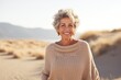 © Markus Schröder - Portrait of a cheerful woman in her 60s wearing a cozy sweater isolated on serene dune landscape background