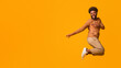 © Prostock-studio - Cheerful young black man having fun over orange background, jumping in the air and showing tricks